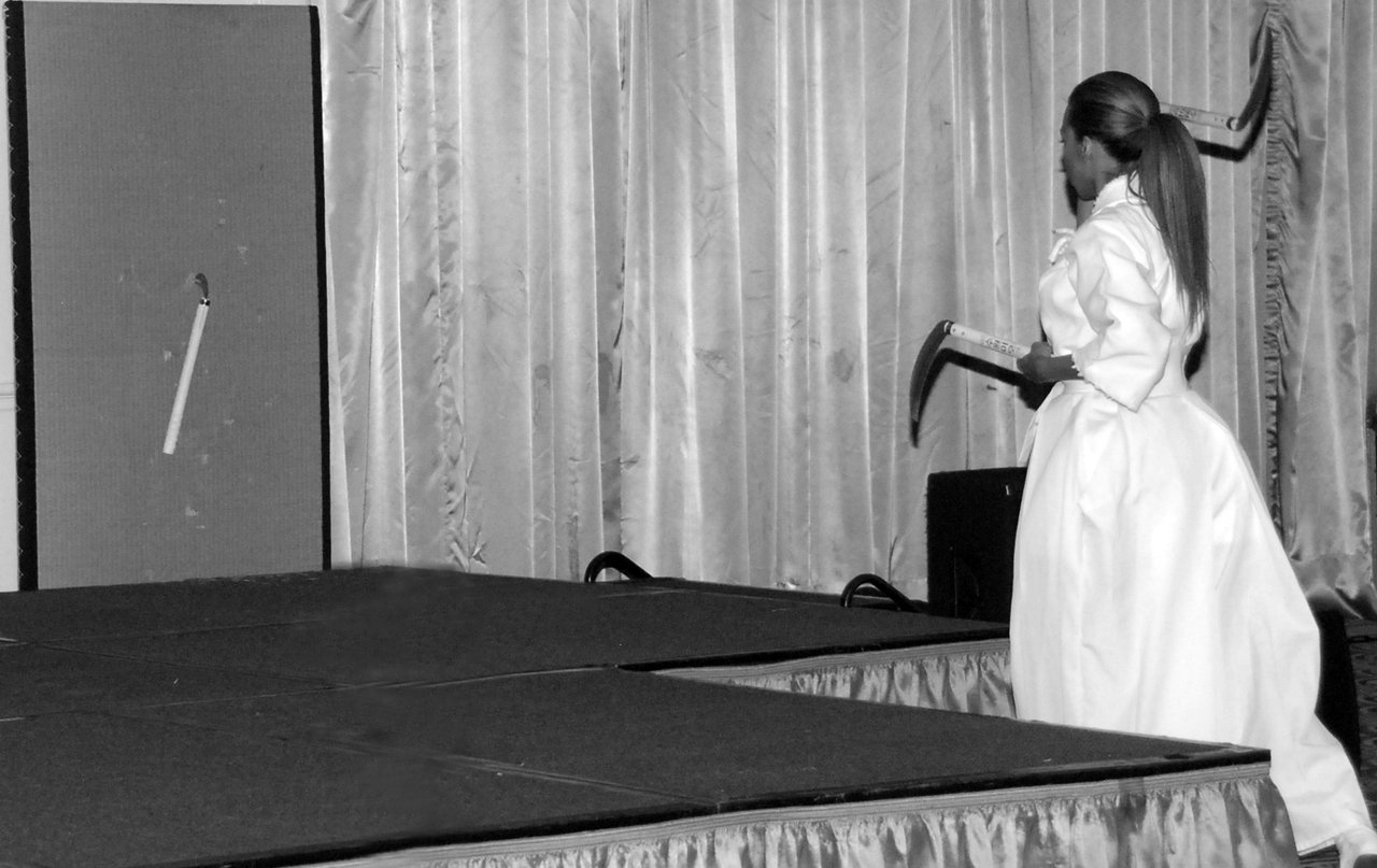 Daisi Pollard demonstrating blade throwing on stage in a white martial arts uniform