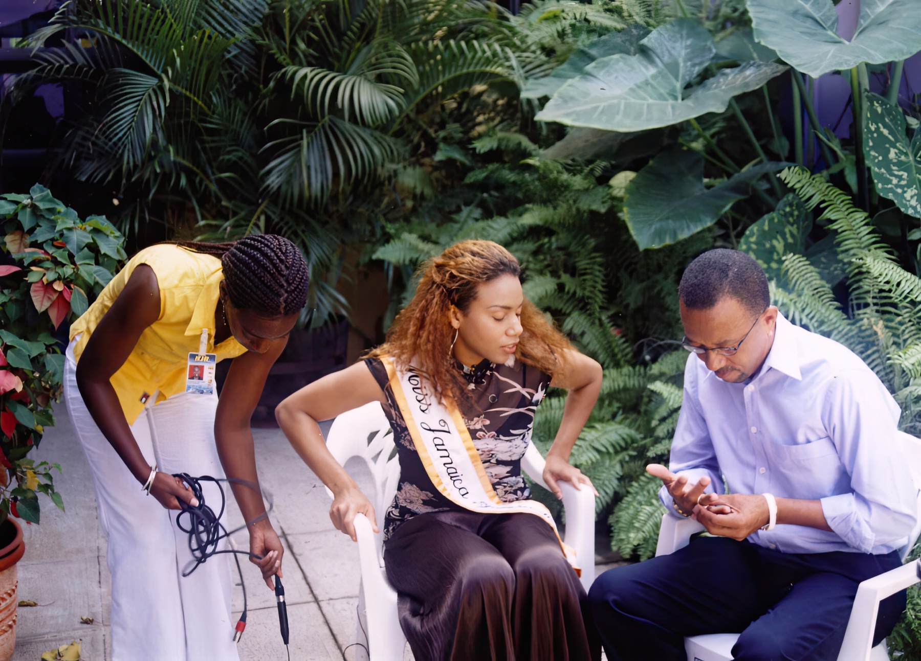 Daisi wearing her Miss Jamaica International sash as a crew prepares for an outdoor interview.